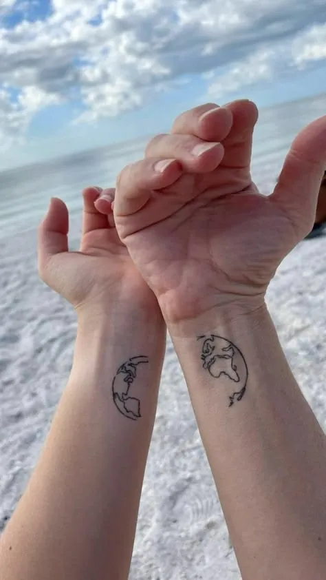 Matching small globe tattoos on two wrists