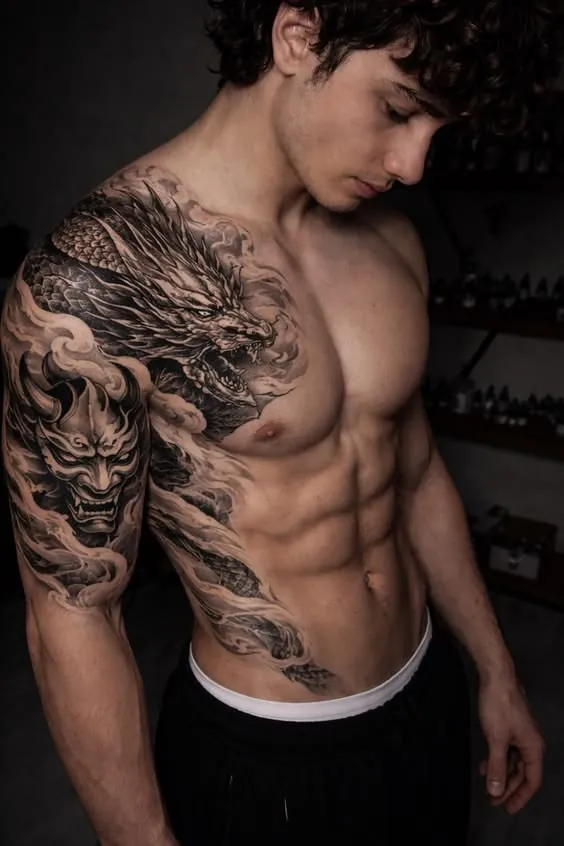 Black and grey dragon and oni mask tattoo across the chest and shoulder
