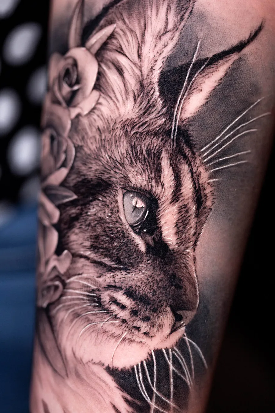 Black and grey realism tattoo of a lynx face with roses on a forearm